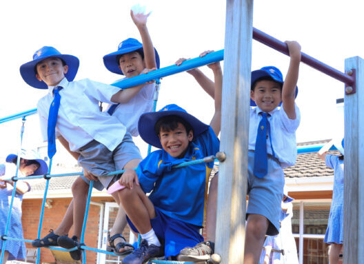 Four young boys in school uniform climbing on a jungle gym and smiling at the camera.