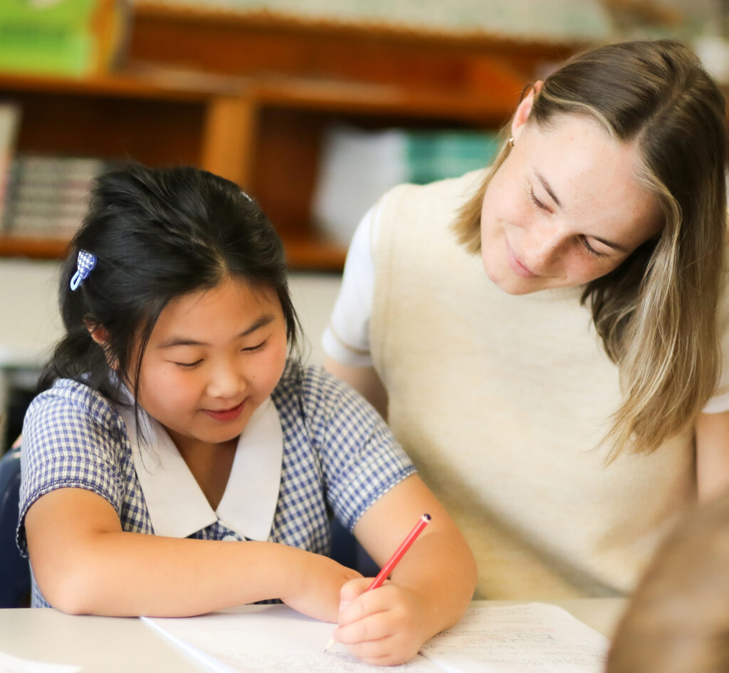 Teacher watches young student as she writes