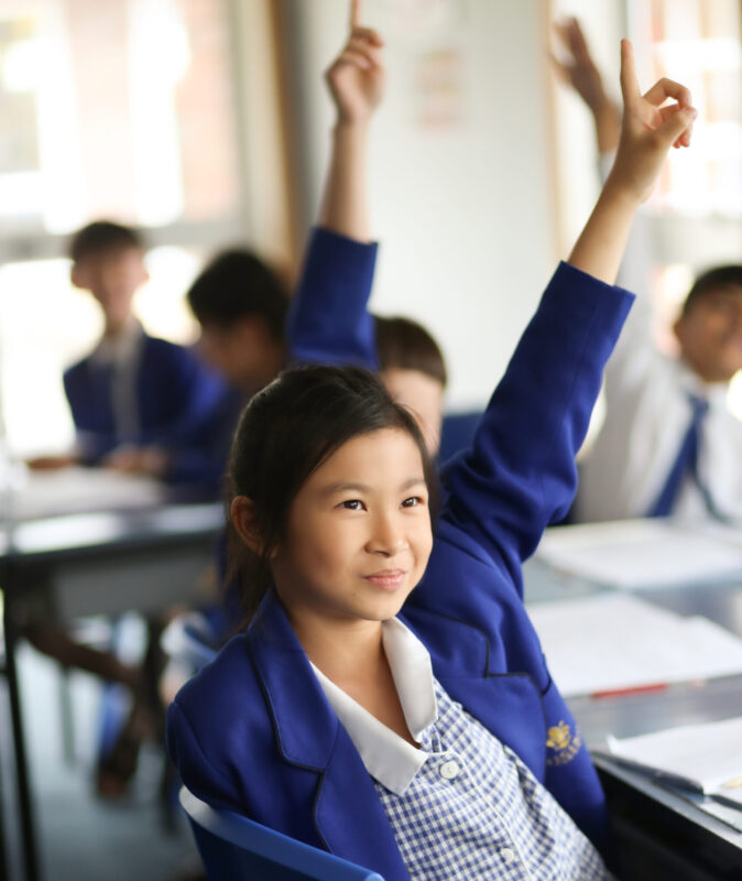 Young primary school student raising her hand in class