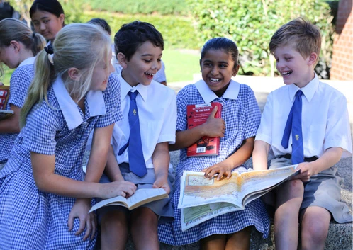 Four primary school children laughing together and holding books.