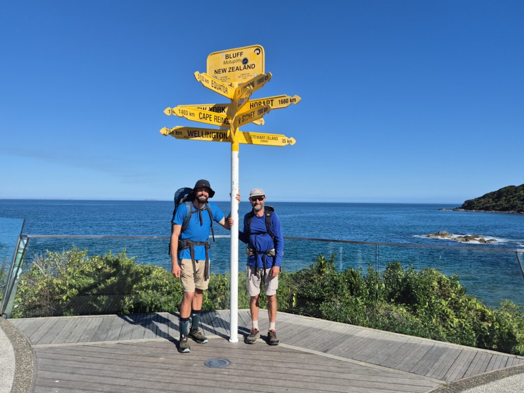 Two men stand at sign in Cape Reinga New Zealand