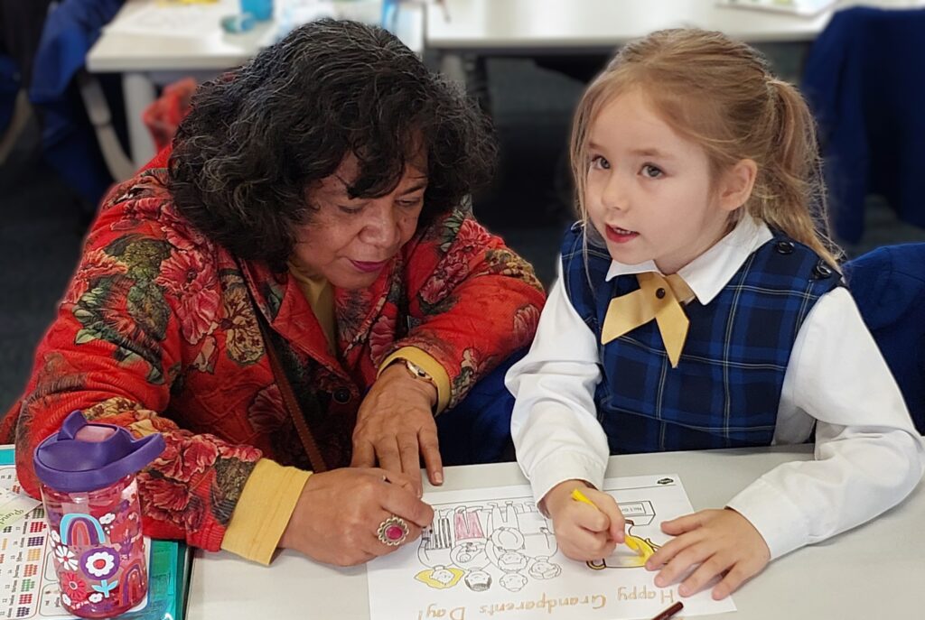 Young girl and adult colouring picture on class desk