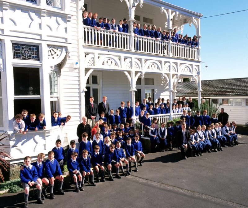 a group of children in blue uniforms in front of an old white villa