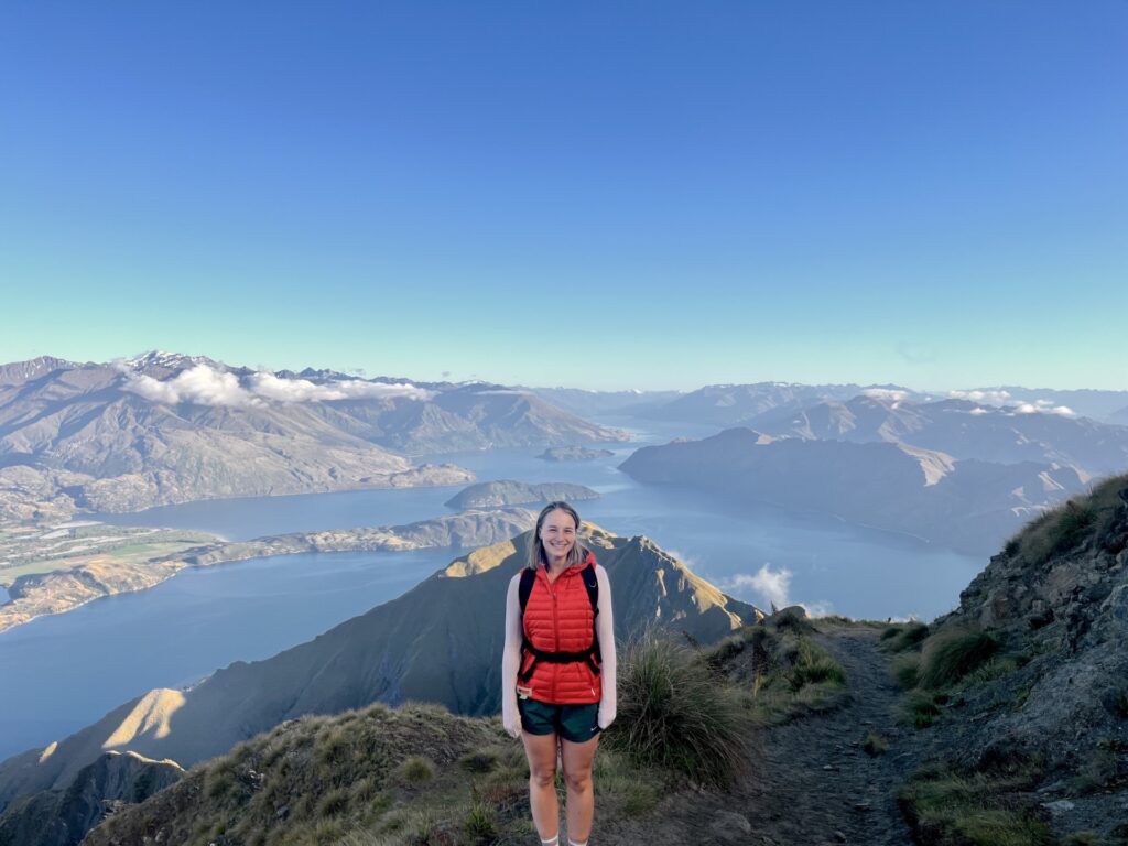 a woman standing on a trail with a body of water in the background