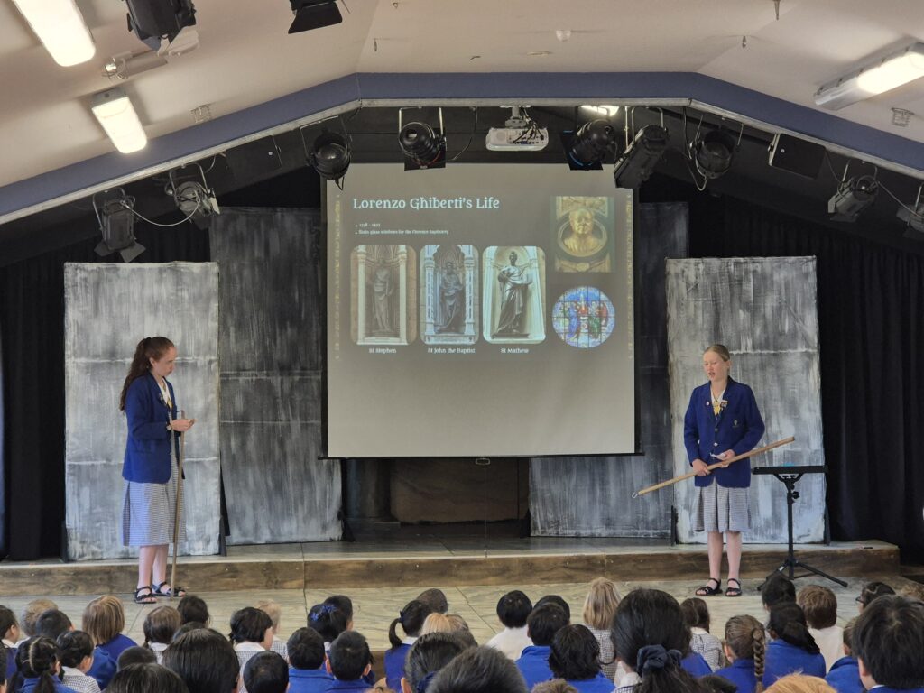 Two school girls giving a presentation in front of an audience.