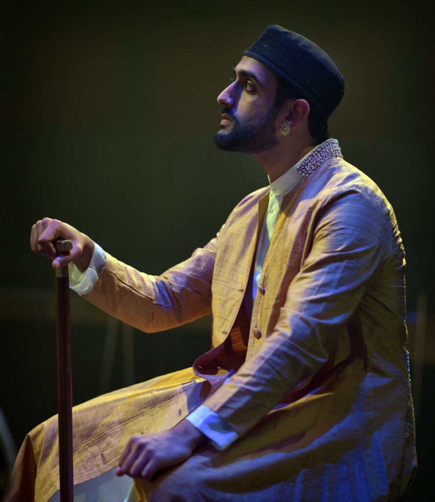 An Indian man wearing a hat and holding a stick.