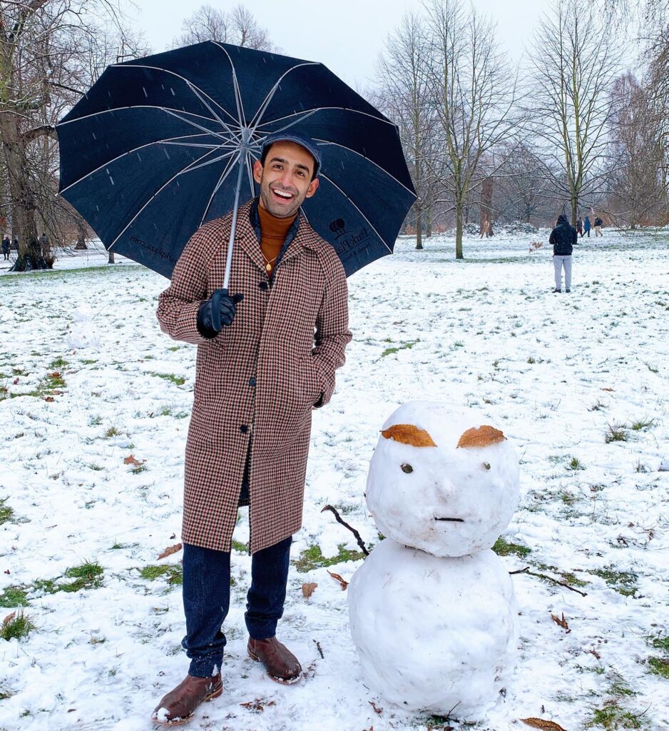 Man with umbressla standing next to a snowman