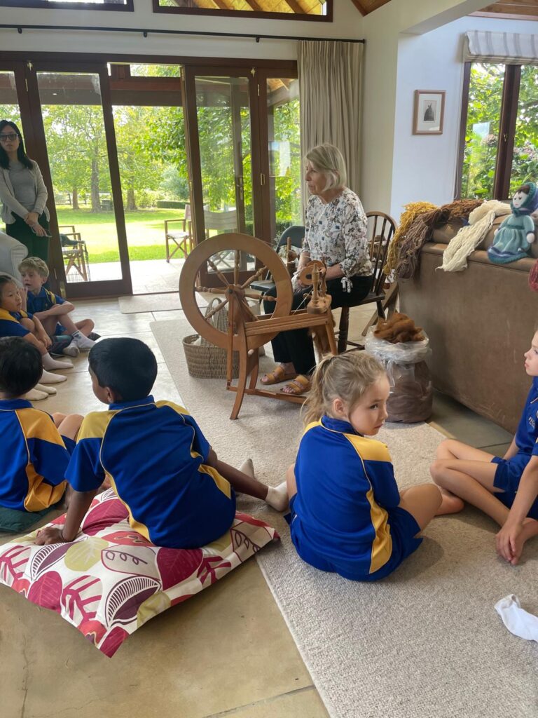 Children watching a woman spin wool