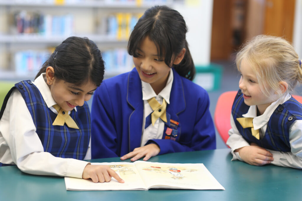 3 school girls reading a book.