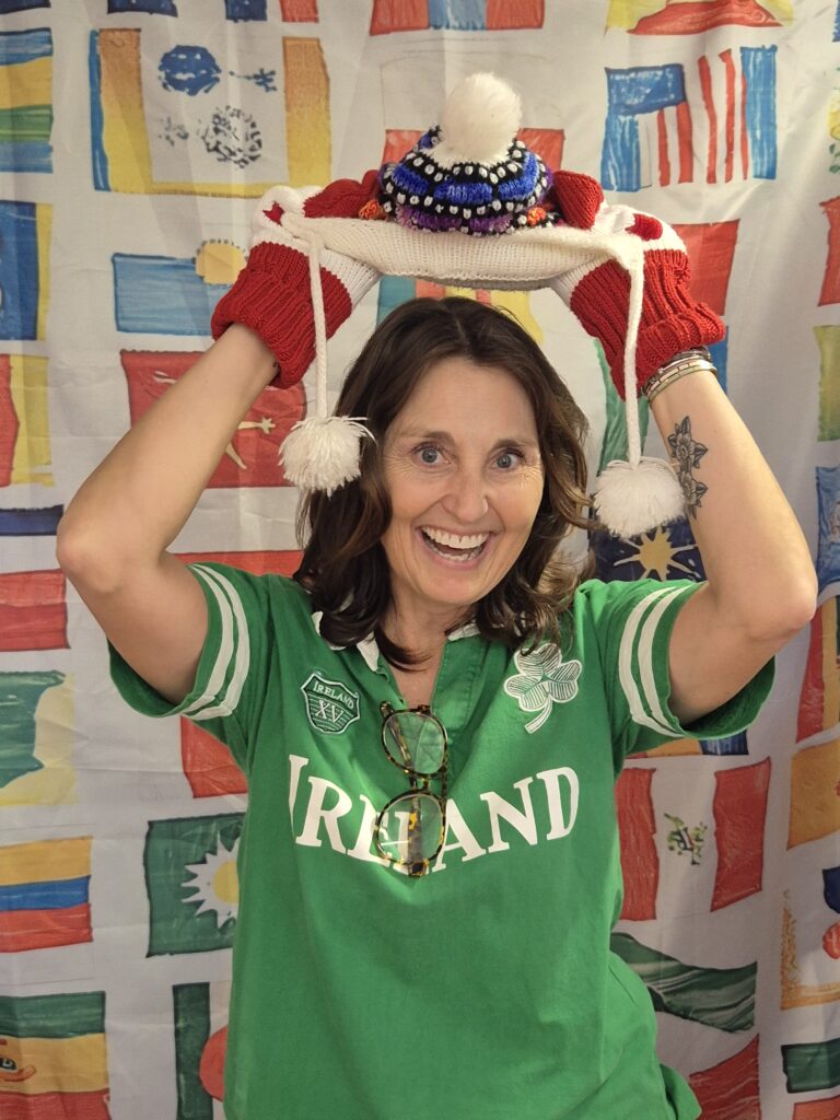 A smiling woman in a green shirt holding a hat above her head