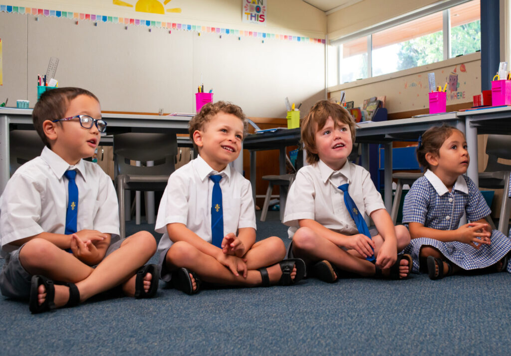 Four young school chldren sitting cross legged on the floor in a classroom