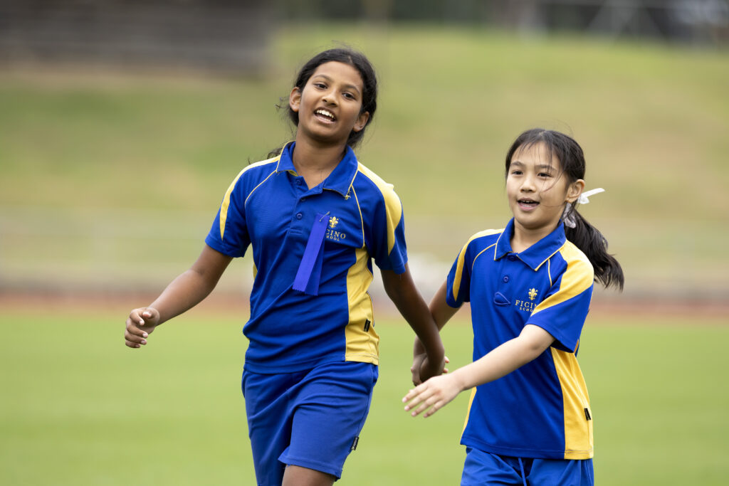 Two school girls wearing blue and yellow sportswear holding hands