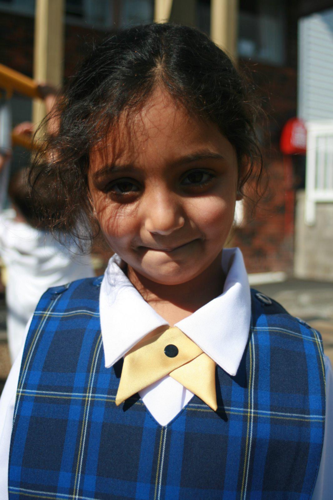 A young Indian schoolgirl wearing a blue, checked pinafore dress